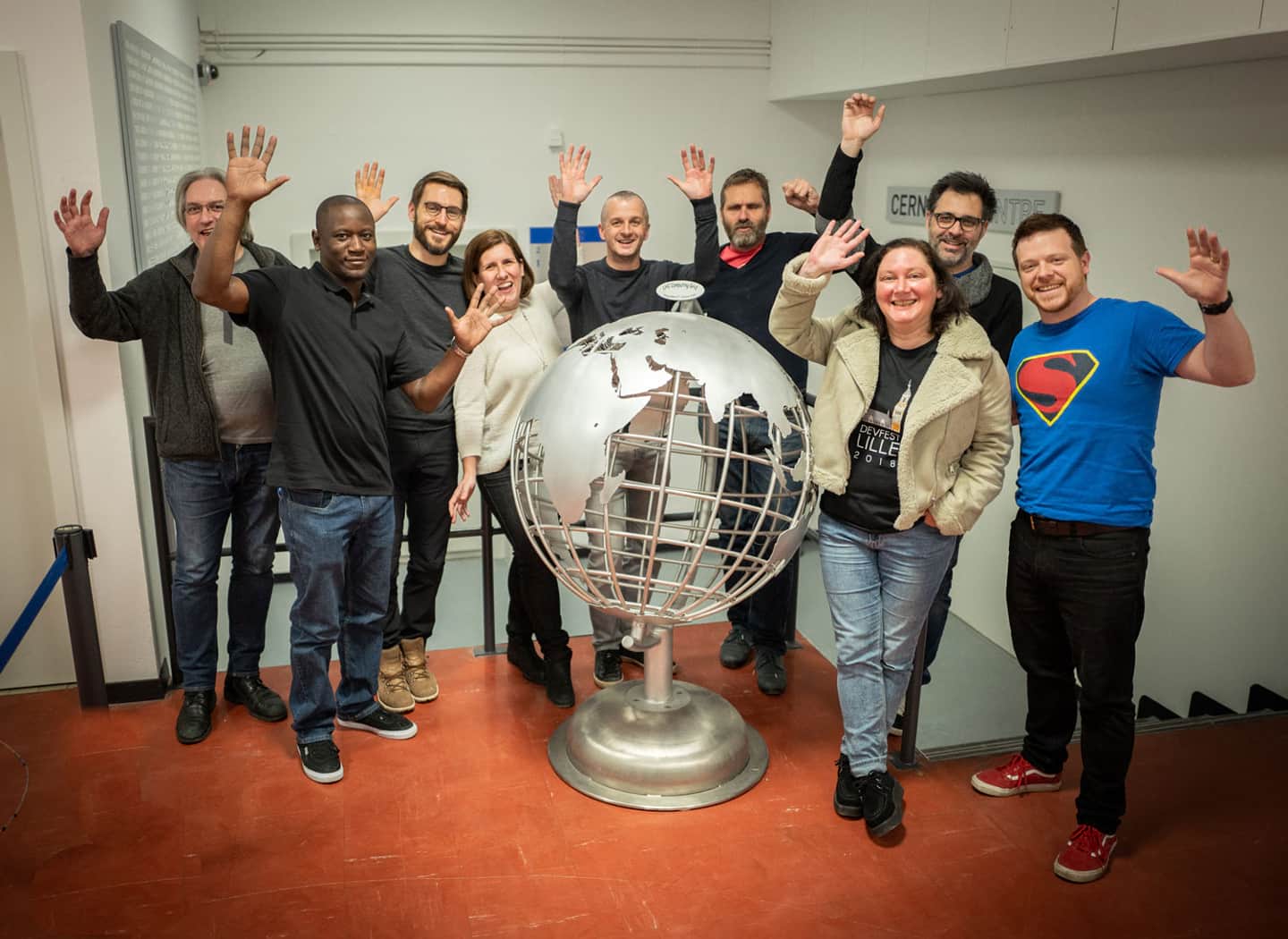 Two women and seven men stand behind a metallic sculpture of the globe showing the continents, many of the people ahve their hands raised