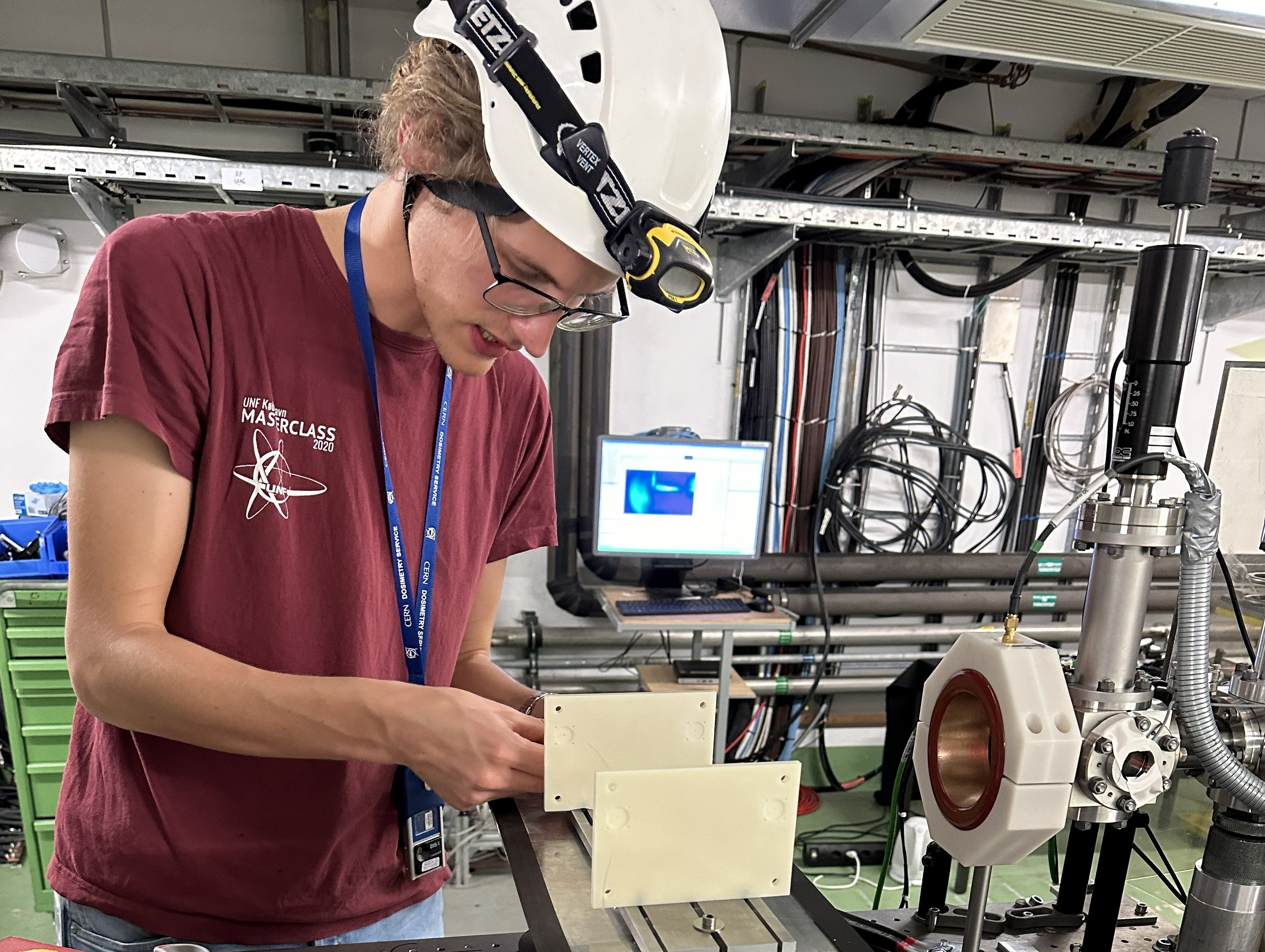 A scientist with a white helmet positioning an optic fibre on a support in an industrial hall