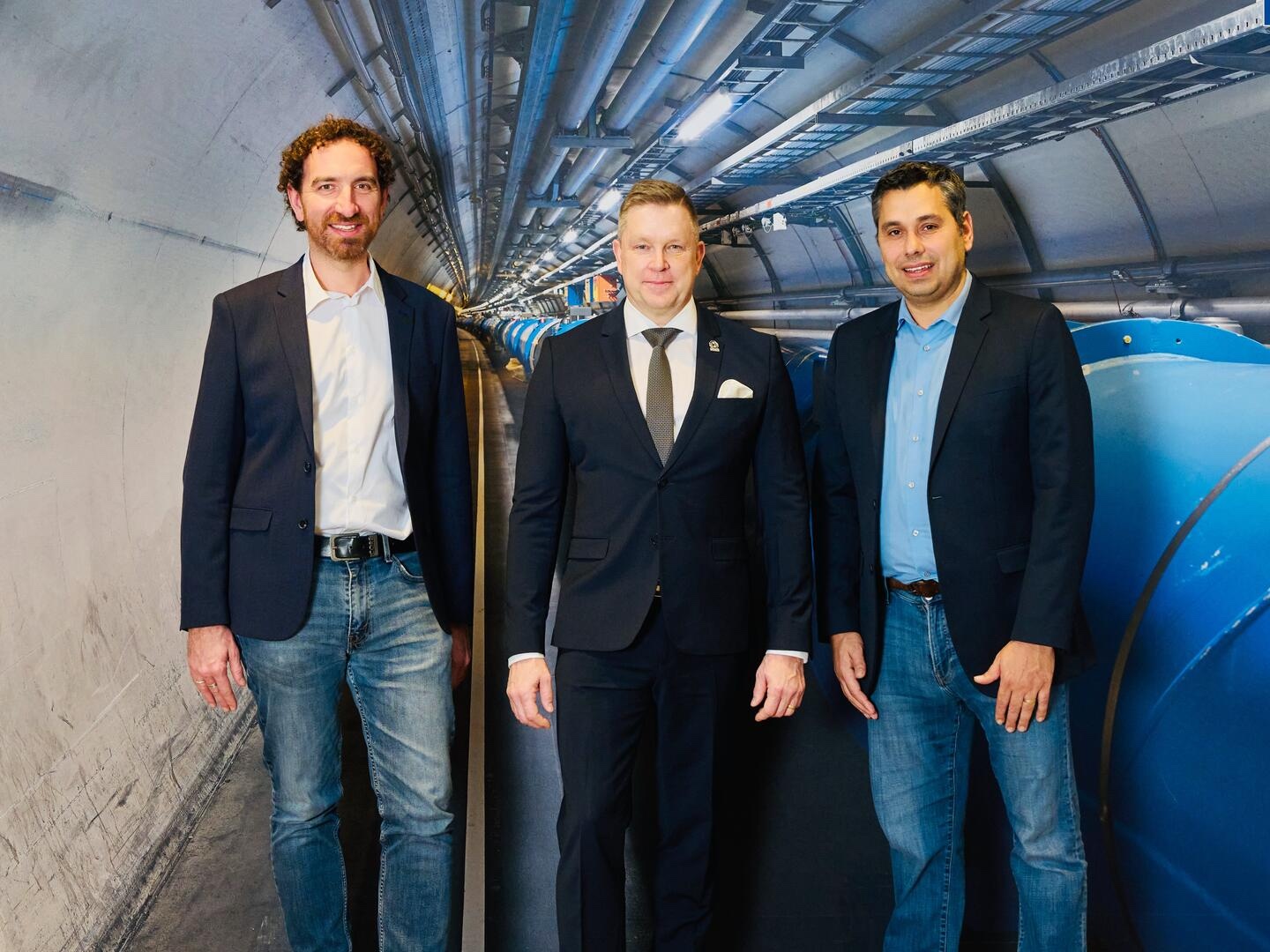 Three men standing in front of a background image of the LHC