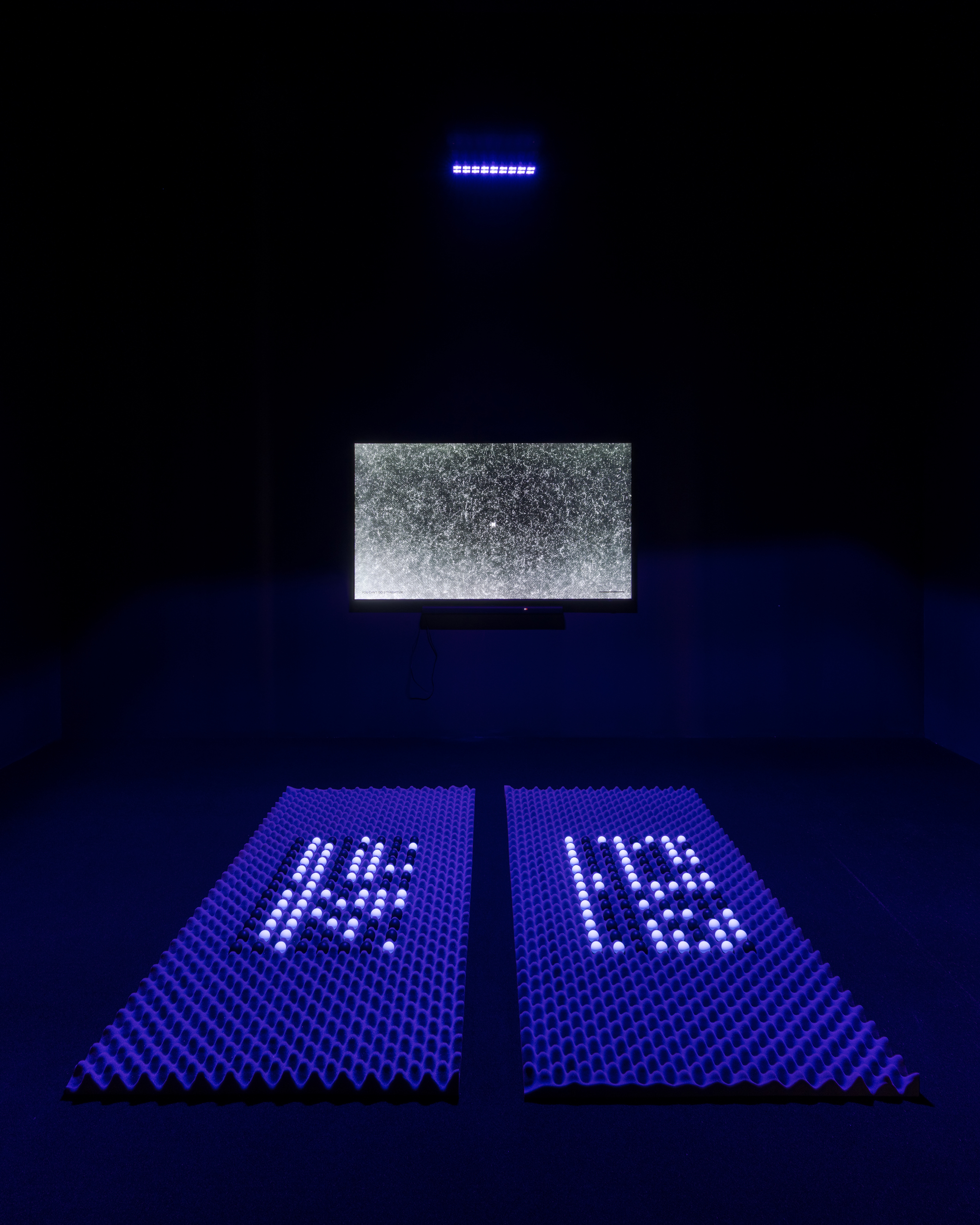 A TV screen in a dark room shows static. In front of the screen, there are black and white balls laid out in a grid