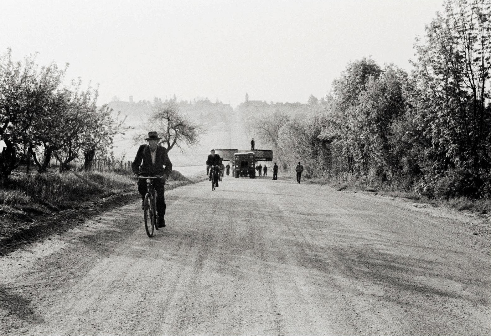 Bikes and a truck with a giant magnet travelling on a country road